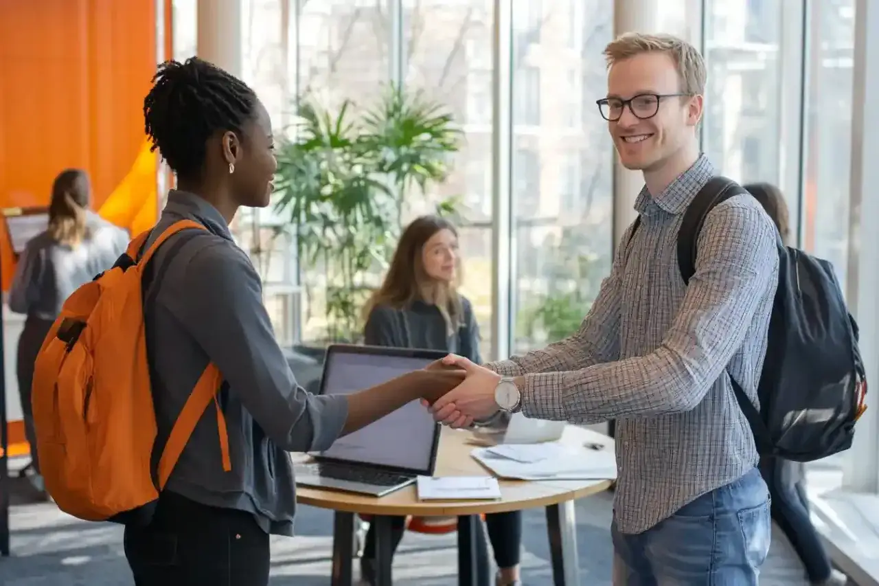 Zwei Studierende mit Rucks&auml;cken sch&uuml;tteln sich die H&auml;nde. Ein Mann mit Brille und eine Frau mit Dreadlocks freuen sich &uuml;ber ihr Praxissemester im Ausland.