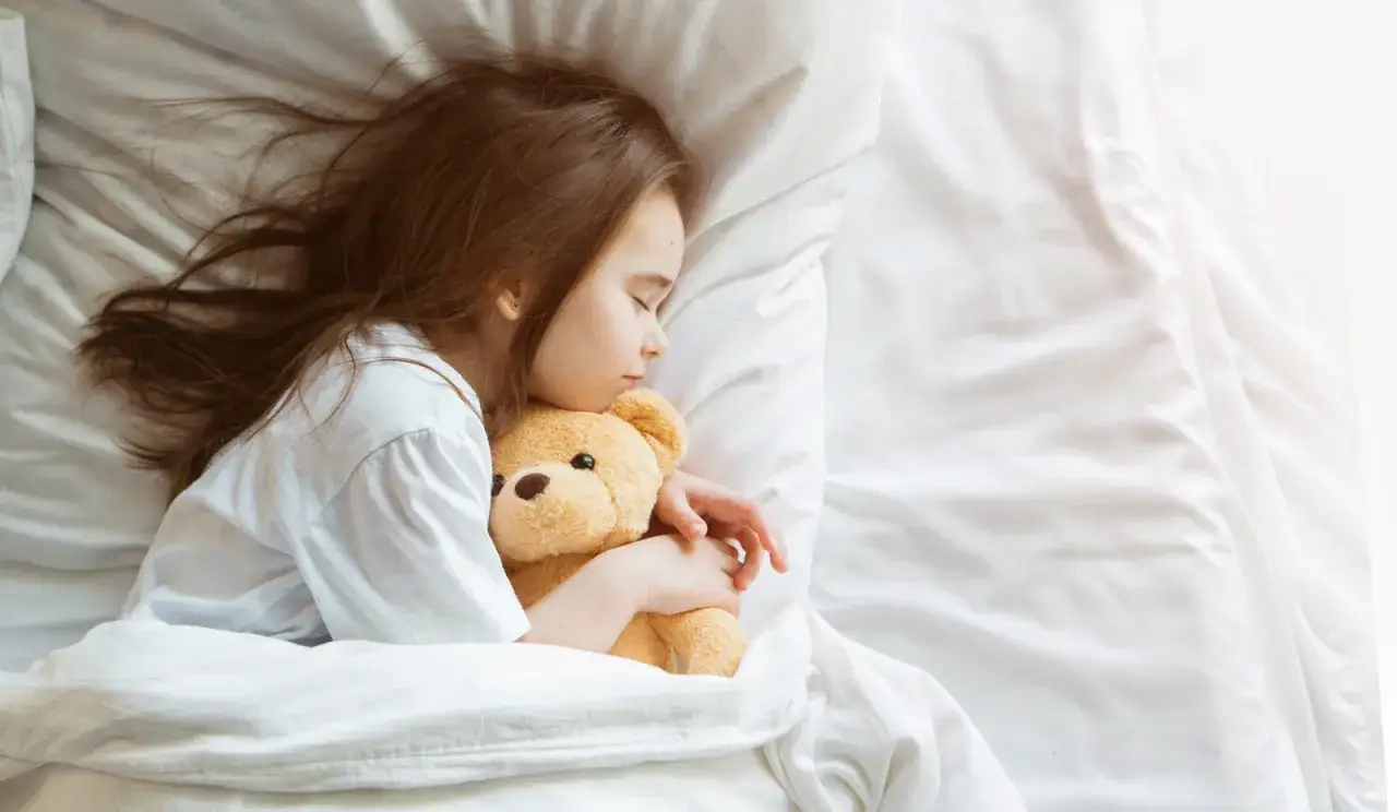 Ein kleines M&auml;dchen schl&auml;ft friedlich mit seinem Teddyb&auml;r. Der Schlafbedarf eines 2-J&auml;hrigen ist wichtig f&uuml;r seine Entwicklung.