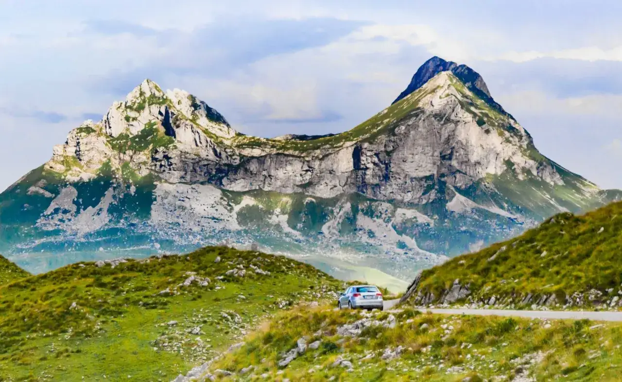 Ein silbernes Auto f&auml;hrt auf einer Stra&szlig;e durch die bergige Landschaft Montenegros. Ein perfekter Montenegro roadtrip!