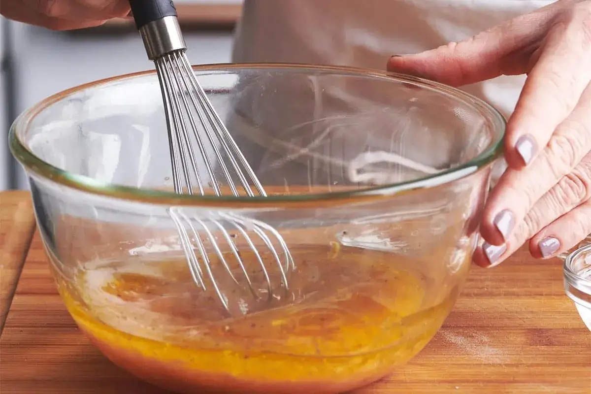 Préparation d'une recette vinaigrette moutarde. Un fouet mélange des ingrédients dans un bol en verre.