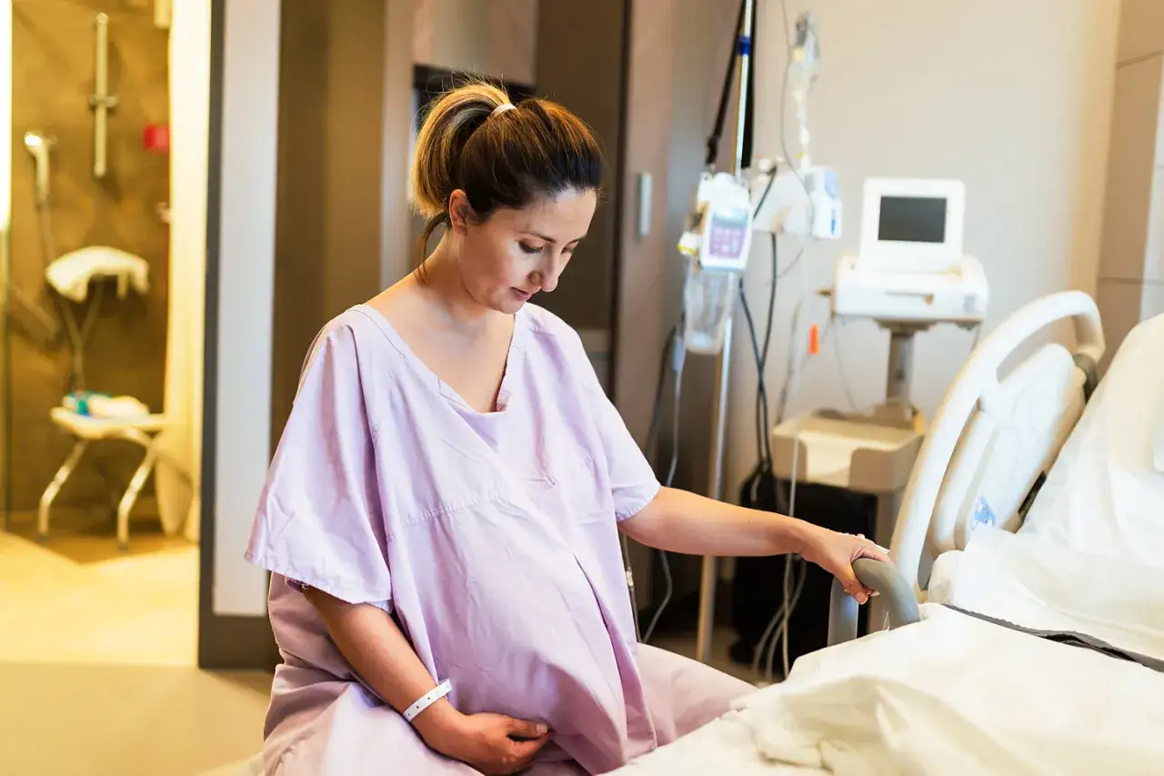 Schwangere Frau im Krankenhaus, die sich fragt, wann platzt die Fruchtblase. Sie sitzt auf dem Bett, umgeben von medizinischen Geräten.