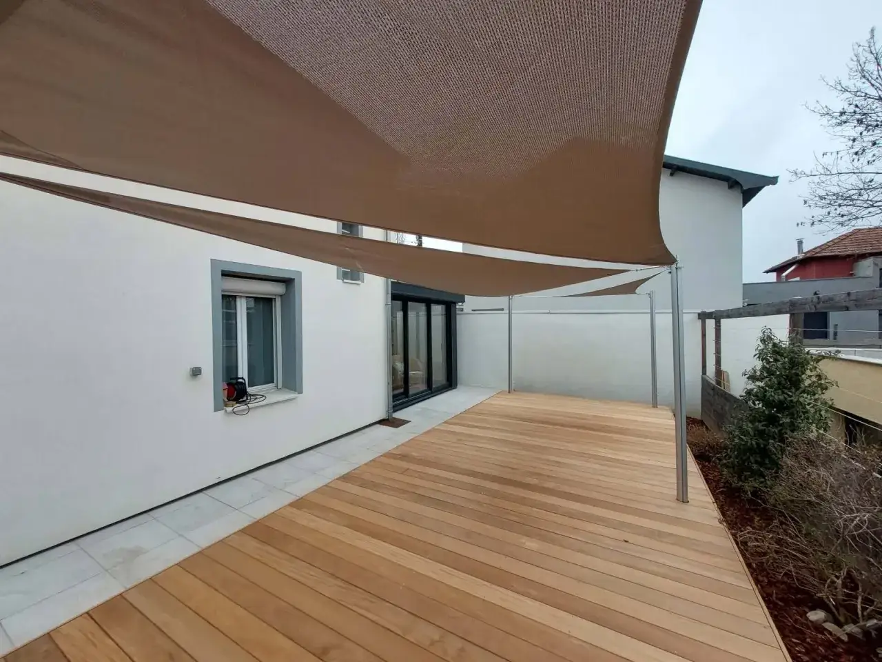 Une terrasse sur pilotis moderne en bois avec un voile d'ombrage brun, offrant un espace extérieur élégant et fonctionnel.
