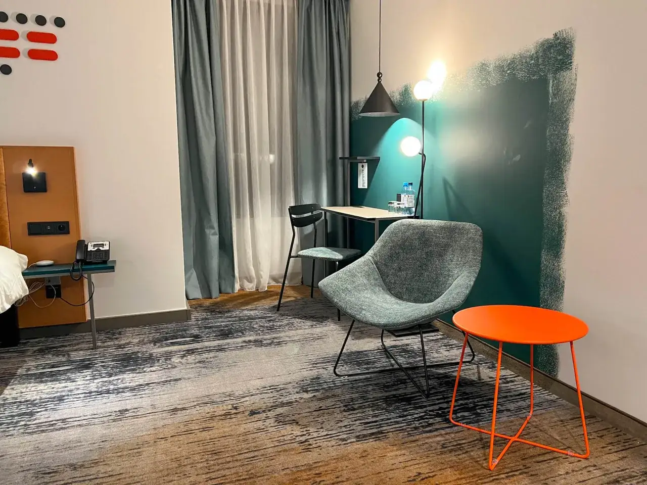 Nowoczesny pokój hotelowy hotel ibis z wygodnym fotelem, biurkiem i pomarańczowym stolikiem.