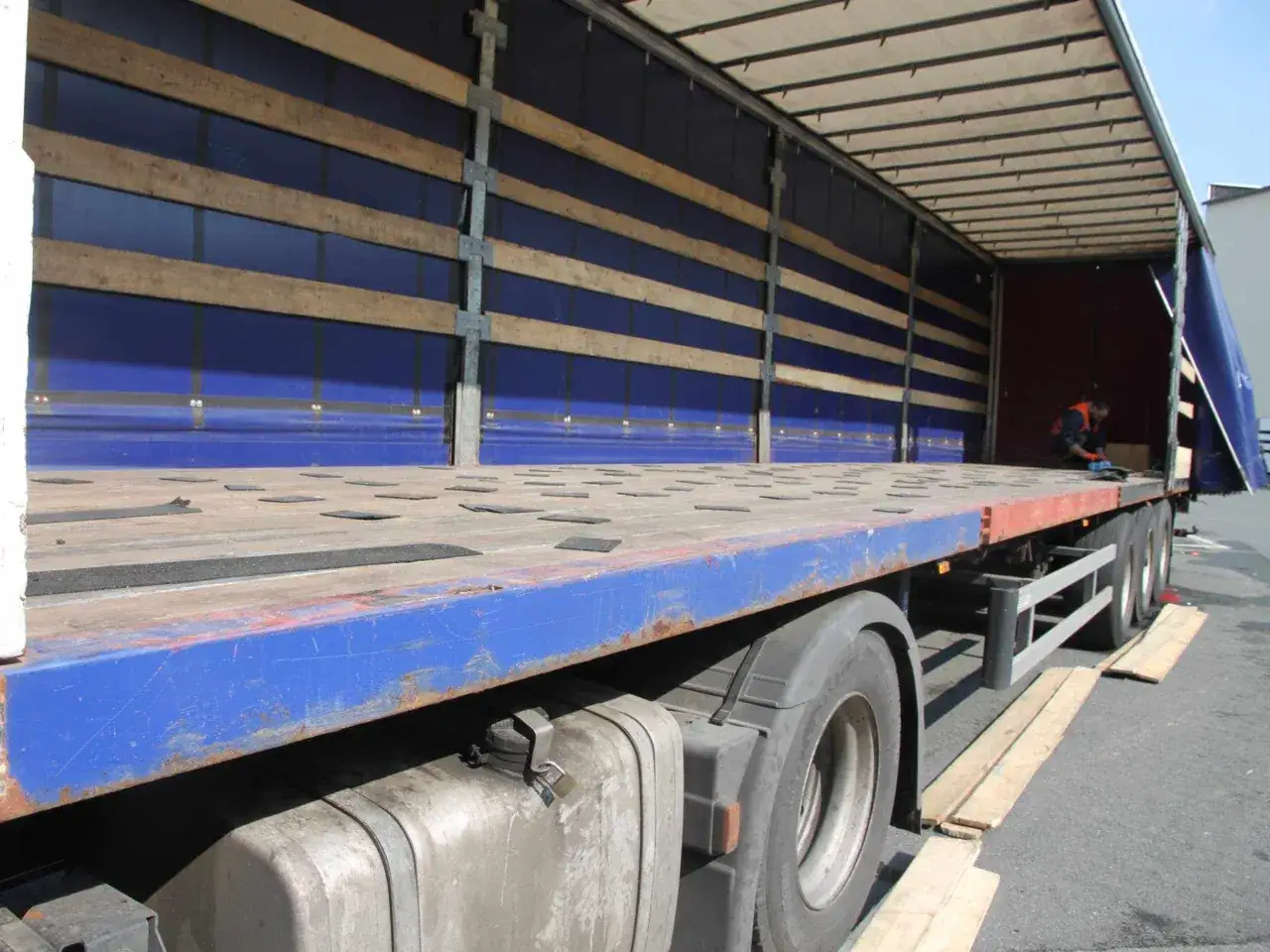 Leerer LKW-Anh&auml;nger mit blauer Plane und Holzlatten. Die Ladefl&auml;che ist frei, bereit f&uuml;r die n&auml;chste Ladung.