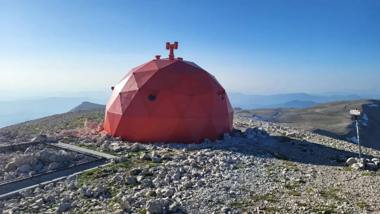 Il rifugio Manzini, una cupola rossa geodetica, si erge su un crinale roccioso sotto un cielo azzurro.