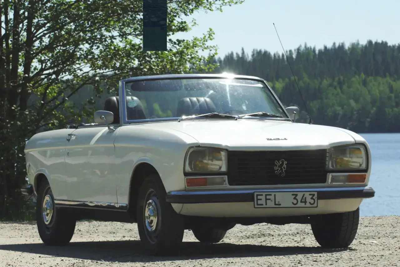 Vit cabriolet Peugeot 304 st&aring;r vid en sj&ouml; med skog i bakgrunden.