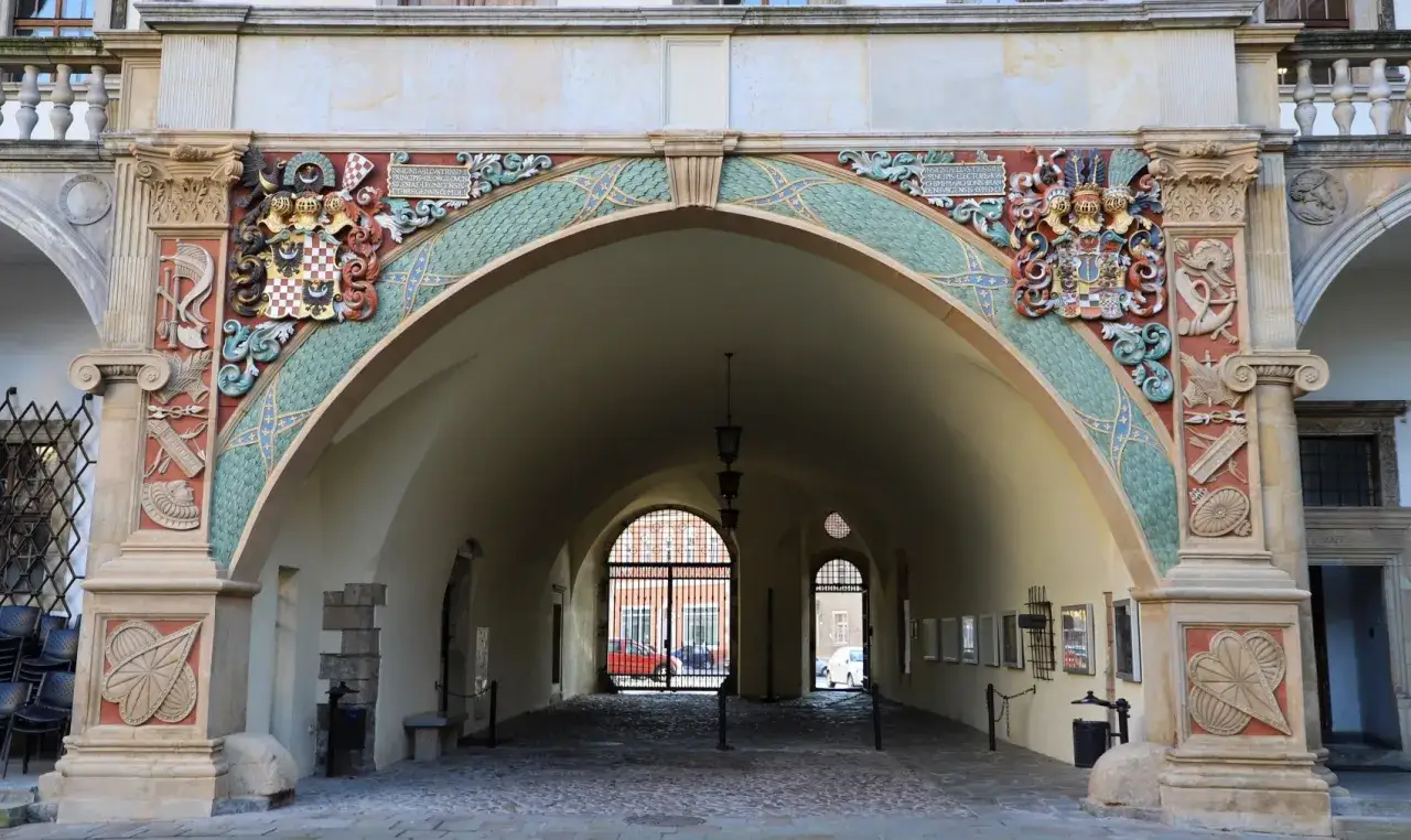 Bogato zdobiony łuk prowadzi do dziedzińca zamku. Herb i ornamenty świadczą o jego historii.