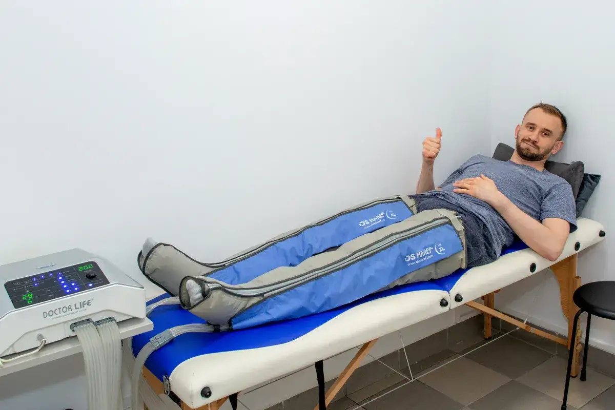 Mężczyzna leży na kozetce, poddając się zabiegowi drenażu limfatycznego n&oacute;g. Pokazuje kciuk w g&oacute;rę, wyrażając zadowolenie.