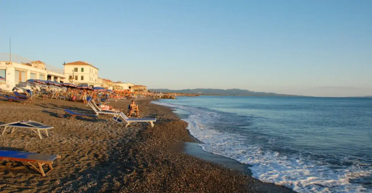 Plage de Cecina Mare au coucher du soleil, avec des chaises longues, des parasols et des b&acirc;timents en bord de mer. L'eau bleue calme rencontre le rivage.