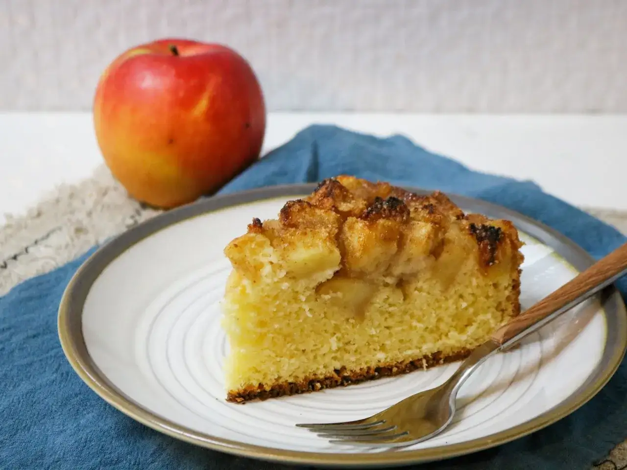 Ein St&uuml;ck von Omas weltbester Apfelkuchen, saftig und mit knuspriger Kruste, daneben ein frischer Apfel.