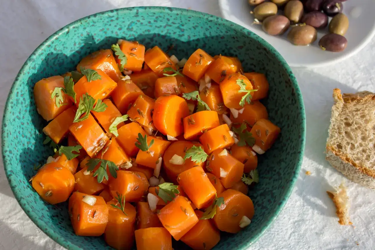 Salade de carottes coupées en dés, assaisonnée de cumin et de persil frais, dans un bol bleu.