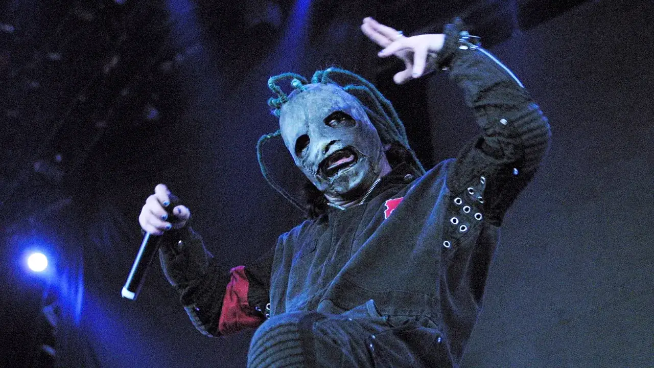 Wokalista w masce z dredami, trzymający mikrofon, w charakterystycznym stroju. To kwintesencja tego, czym jest nu metal.