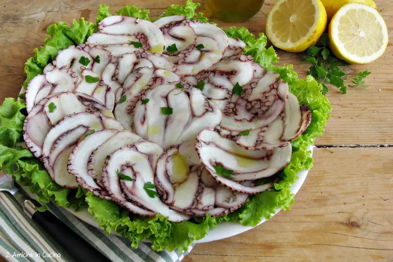 Delicato carpaccio di polpo su letto di lattuga, condito con olio e prezzemolo. Accanto, spicchi di limone fresco.