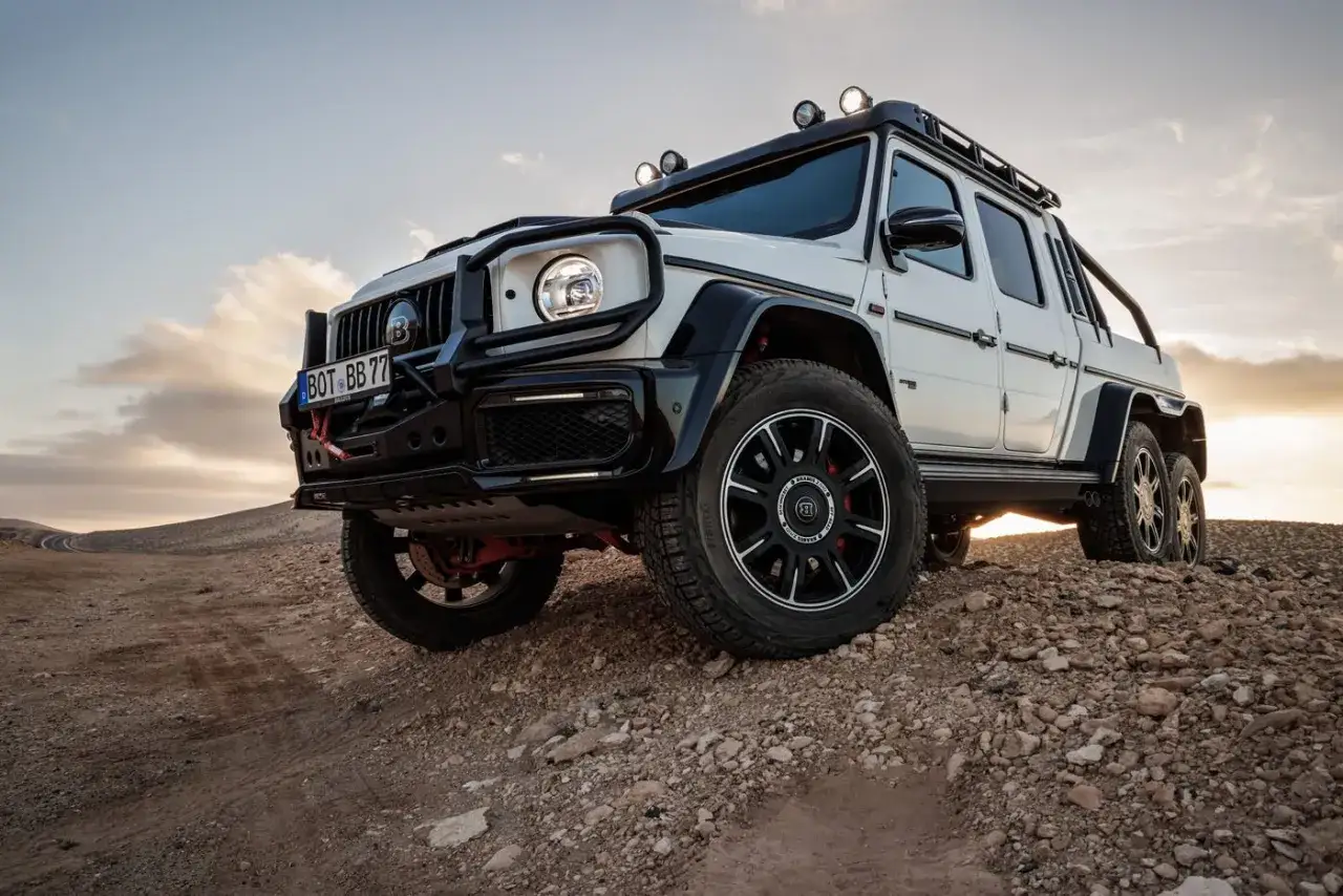 Potężny biały Mercedes 6x6 z terenowym wyposażeniem, gotowy na podbój pustyni o zachodzie słońca.