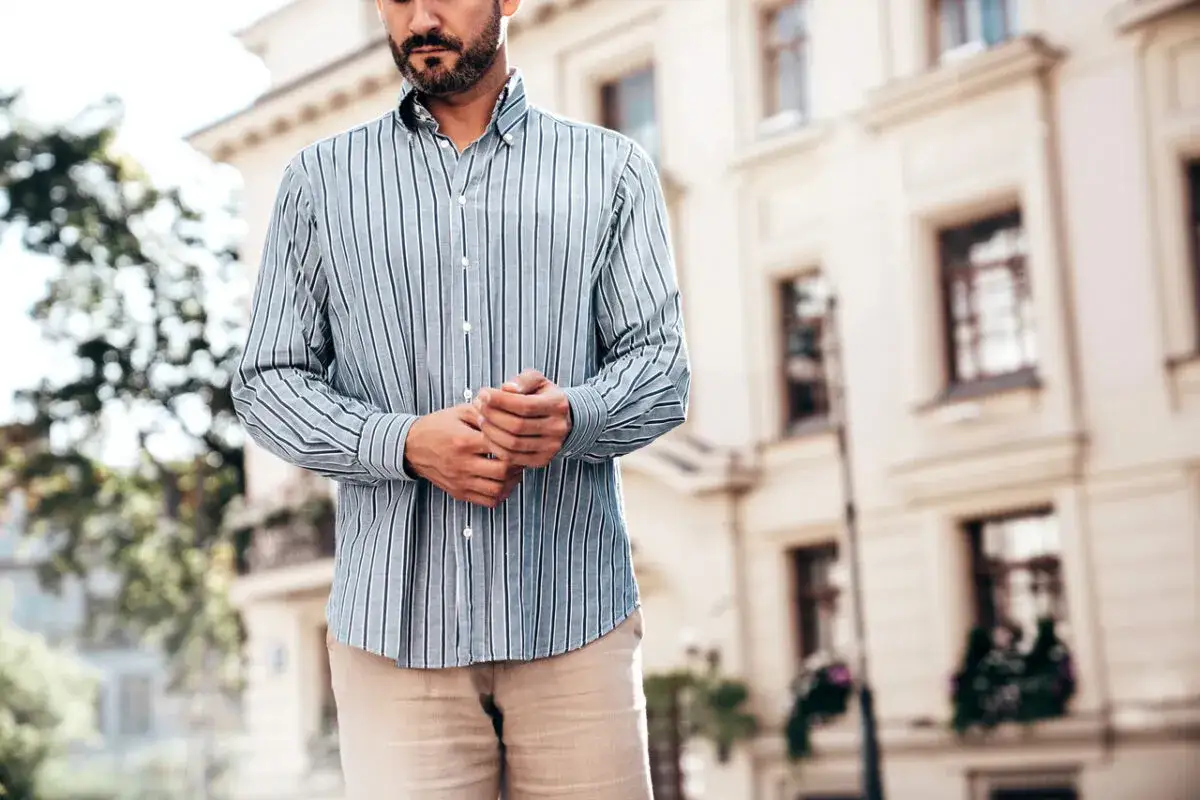 Mężczyzna w paski, jak włożyć koszulę w spodnie, prezentuje elegancki styl na tle kamienicy.