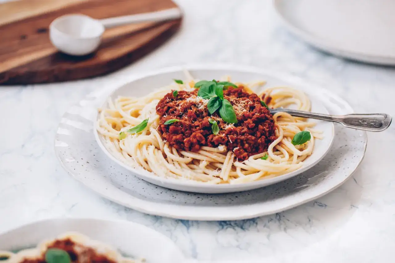 Pyszne spaghetti z sosem bolognese, posypane parmezanem i udekorowane bazylią. Idealne danie dla miłośników włoskiej kuchni.