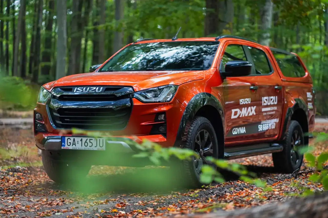 Pomarańczowy Isuzu D-MAX w lesie, gotowy na przygodę.
