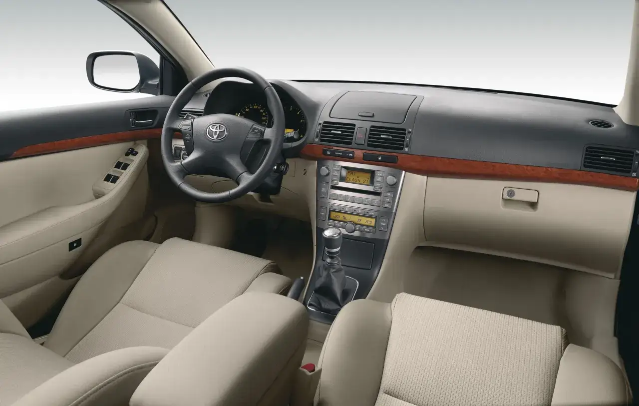 Wnętrze Toyoty Avensis T25: kierownica, deska rozdzielcza z radiem i nawigacją, dźwignia zmiany biegów, jasne fotele.