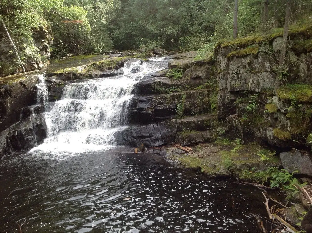 Vattenfall i en skogsmilj&ouml; n&auml;ra Lillehammer, Norge. Mossbekl&auml;dda klippor och m&ouml;rkt vatten.
