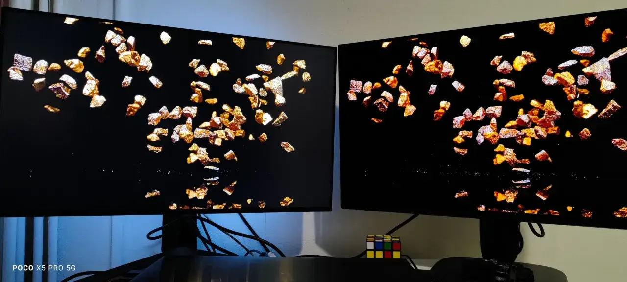 Dwa monitory obok siebie, jeden z technologią OLED, drugi IPS, wyświetlają obraz z płatkami złota na czarnym tle.