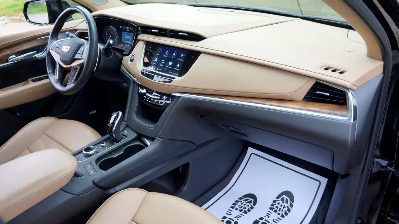 Wnętrze luksusowego **Cadillac XT5** z beżową tapicerką, ekranem dotykowym i drewnianymi wstawkami.