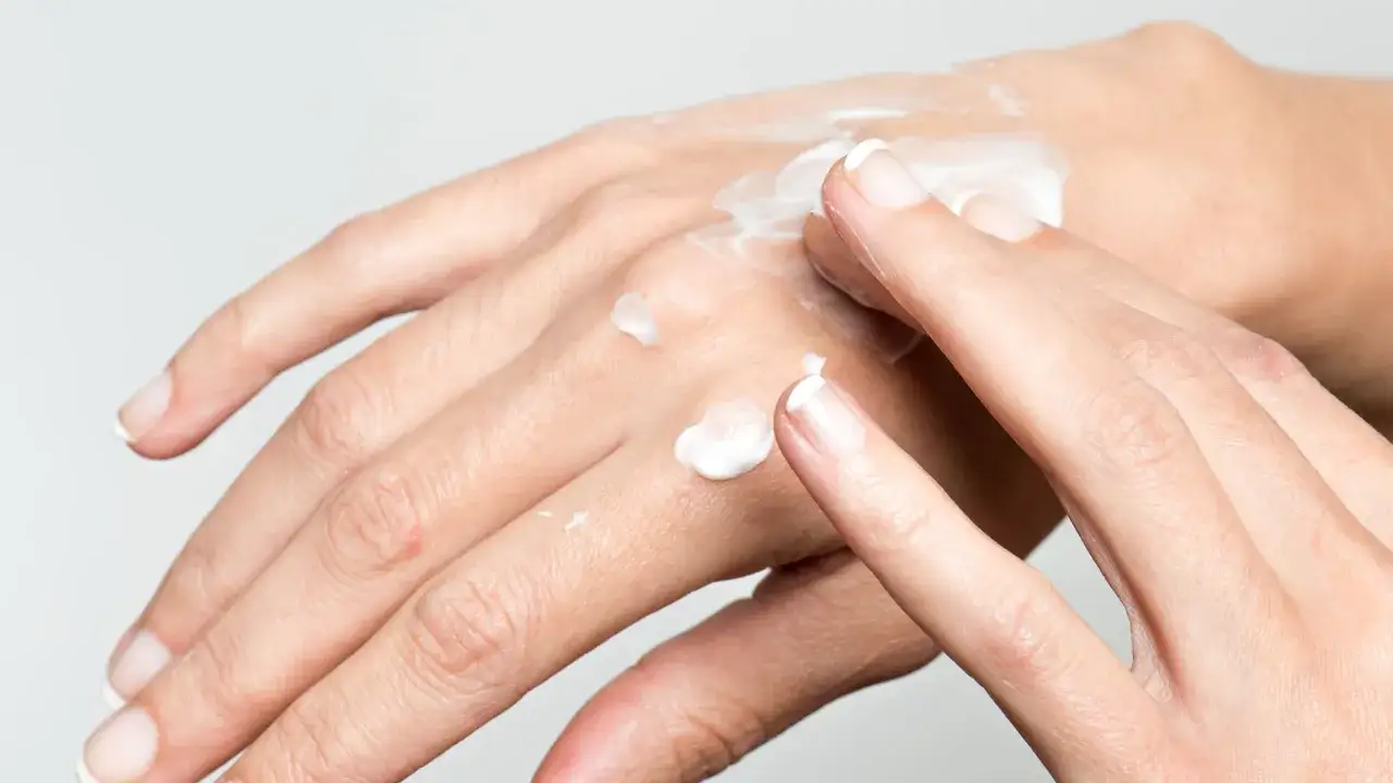 H&auml;nde mit trockenen Fingern werden mit wei&szlig;er Creme eingerieben.