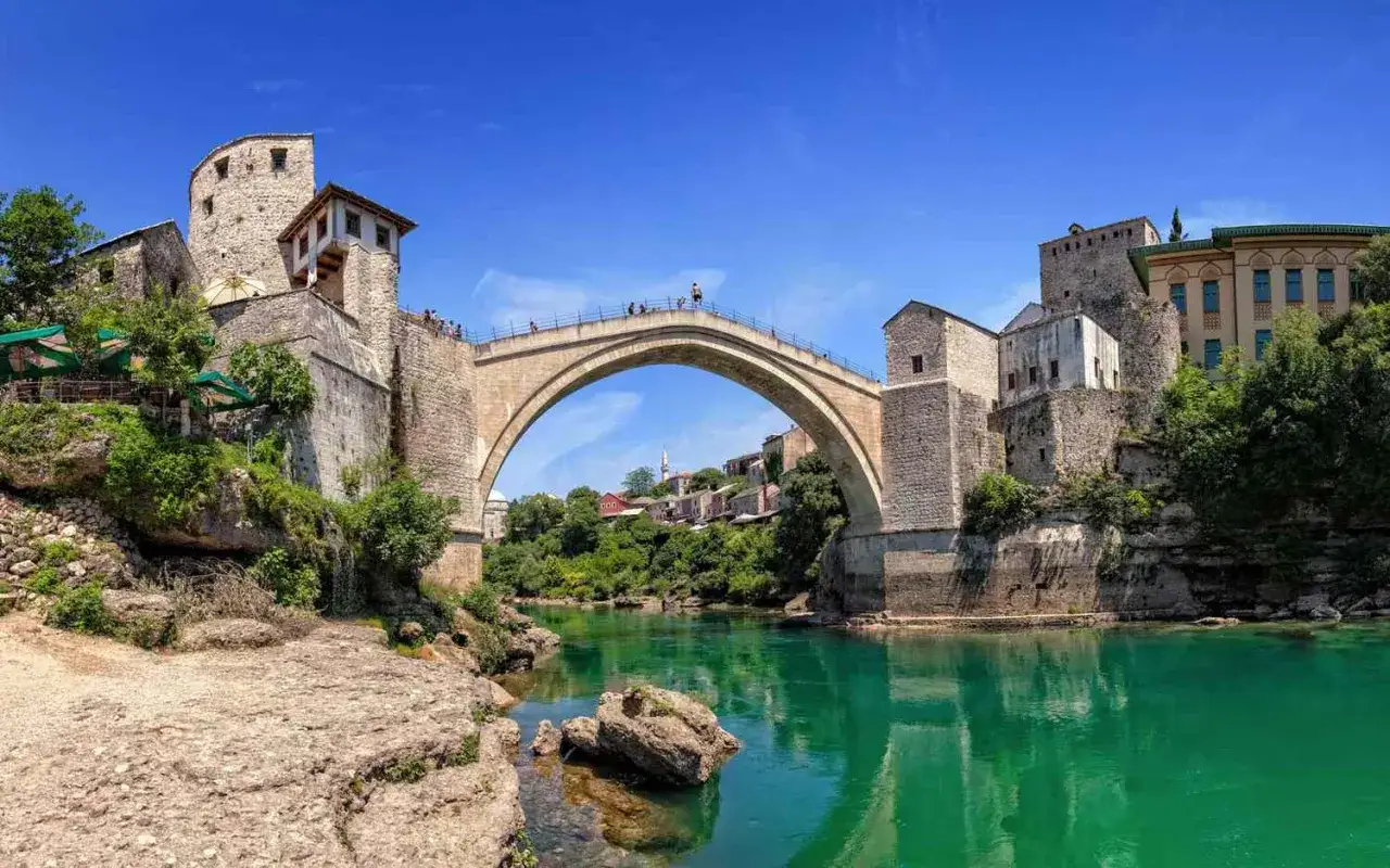 Mostar, jeden z najdziwniejszych mostów świata, łukiem spina turkusową rzekę. Kamienne wieże i zielone dachy tworzą malowniczy krajobraz.