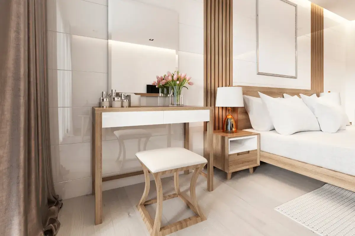 Elegancka toaletka w sypialni inspiracje: nowoczesny mebel z lustrem, kosmetykami i bukietem różowych tulipanów. Obok łóżko i stolik nocny.