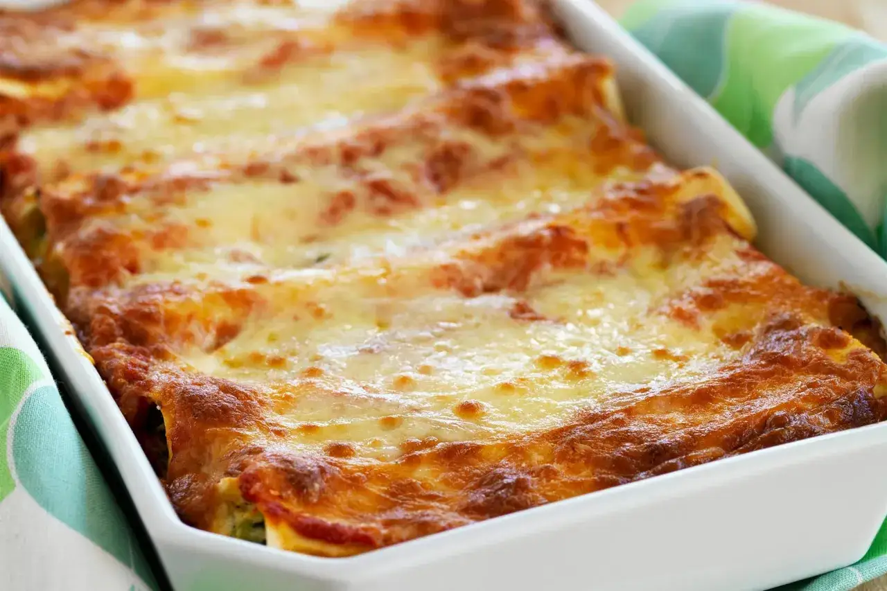 Cannelloni ricotta e spinaci appena sfornati, dorati e filanti, in una teglia bianca con un tovagliolo a fantasia verde.