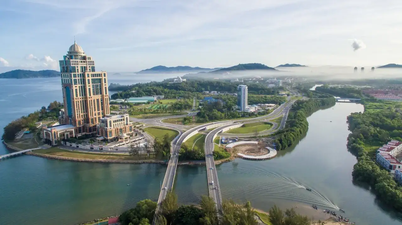 Ein imposantes Geb&auml;ude am Wasser, umgeben von gr&uuml;ner Landschaft und nebligen Bergen. Perfekt f&uuml;r die beste Reisezeit Malaysia.