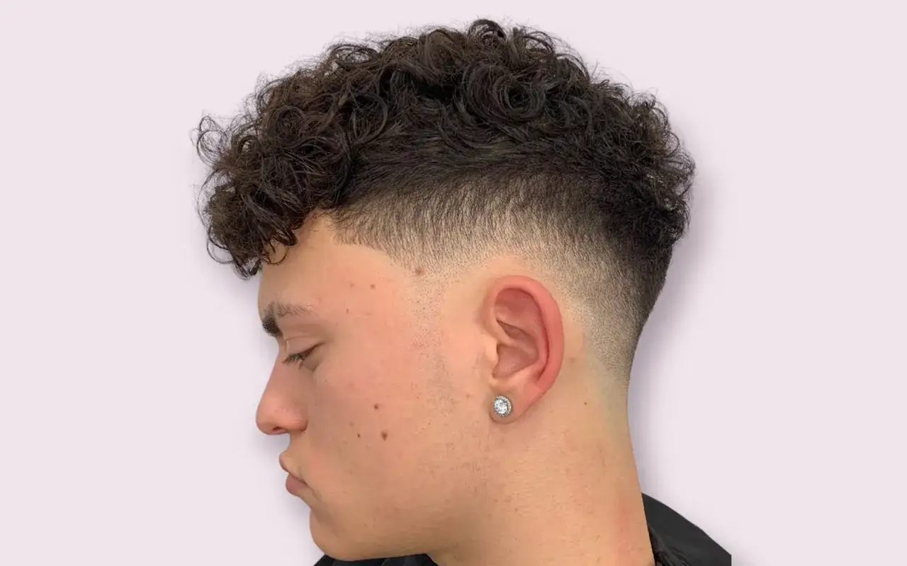Ragazzo con riccioli scuri e sfumatura ai lati. Un esempio di acconciature capelli ragazzo moderne e di tendenza.