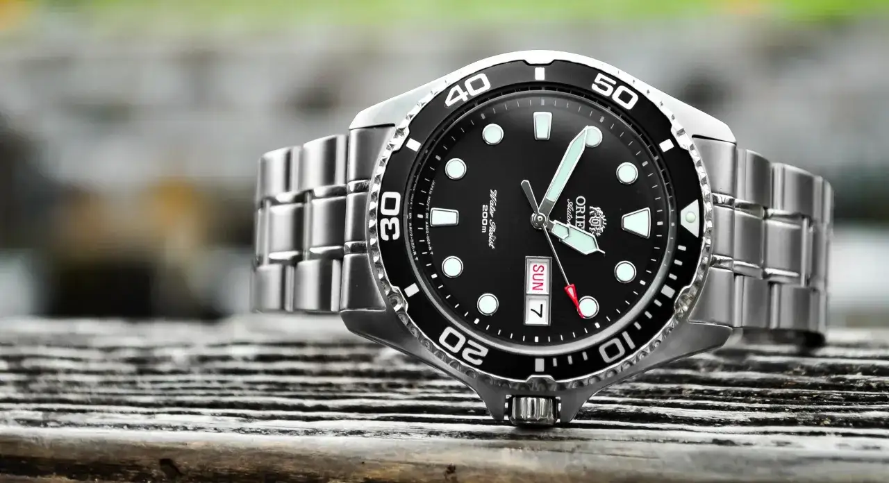 En n&auml;rbild p&aring; en Orient Ray II dykarklocka med svart urtavla och silverf&auml;rgat armband, som ligger p&aring; en tr&auml;yta.