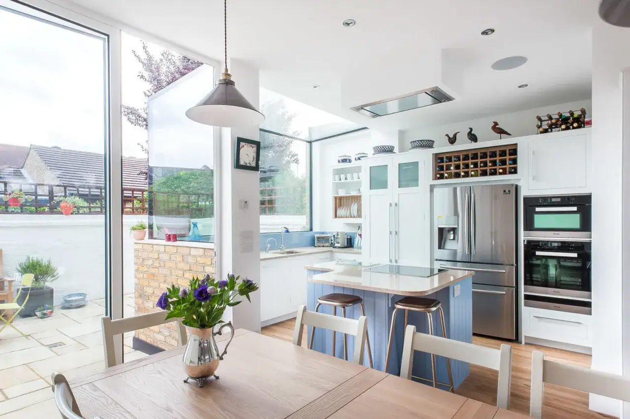 Luminosa cucina moderna con isola centrale e ampie vetrate che si aprono sul giardino. Progetti cucine con porta finestra che massimizzano la luce naturale.