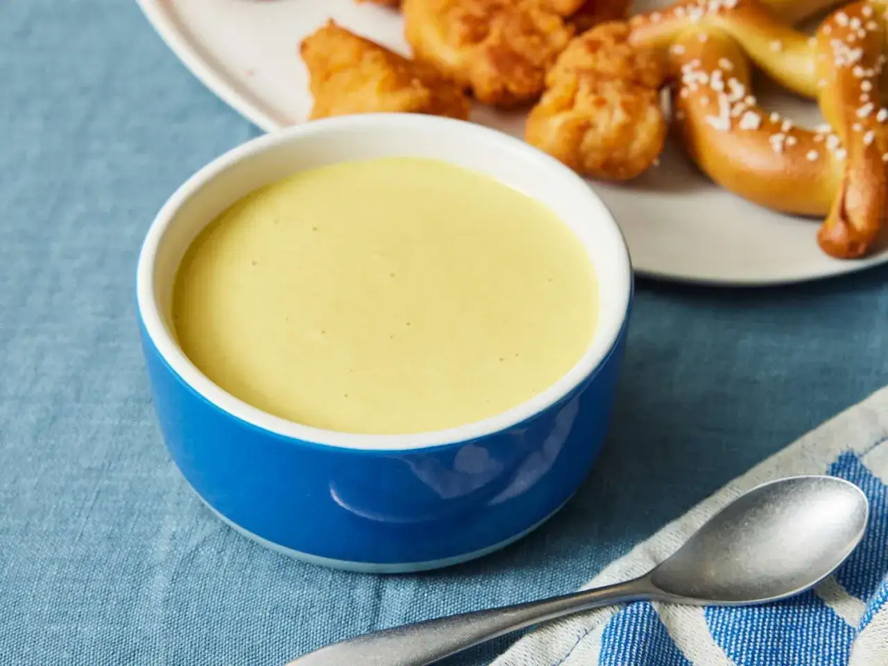 Eine Schüssel cremiger Honig-Senf-Sauce neben knusprigen Nuggets und Brezeln.