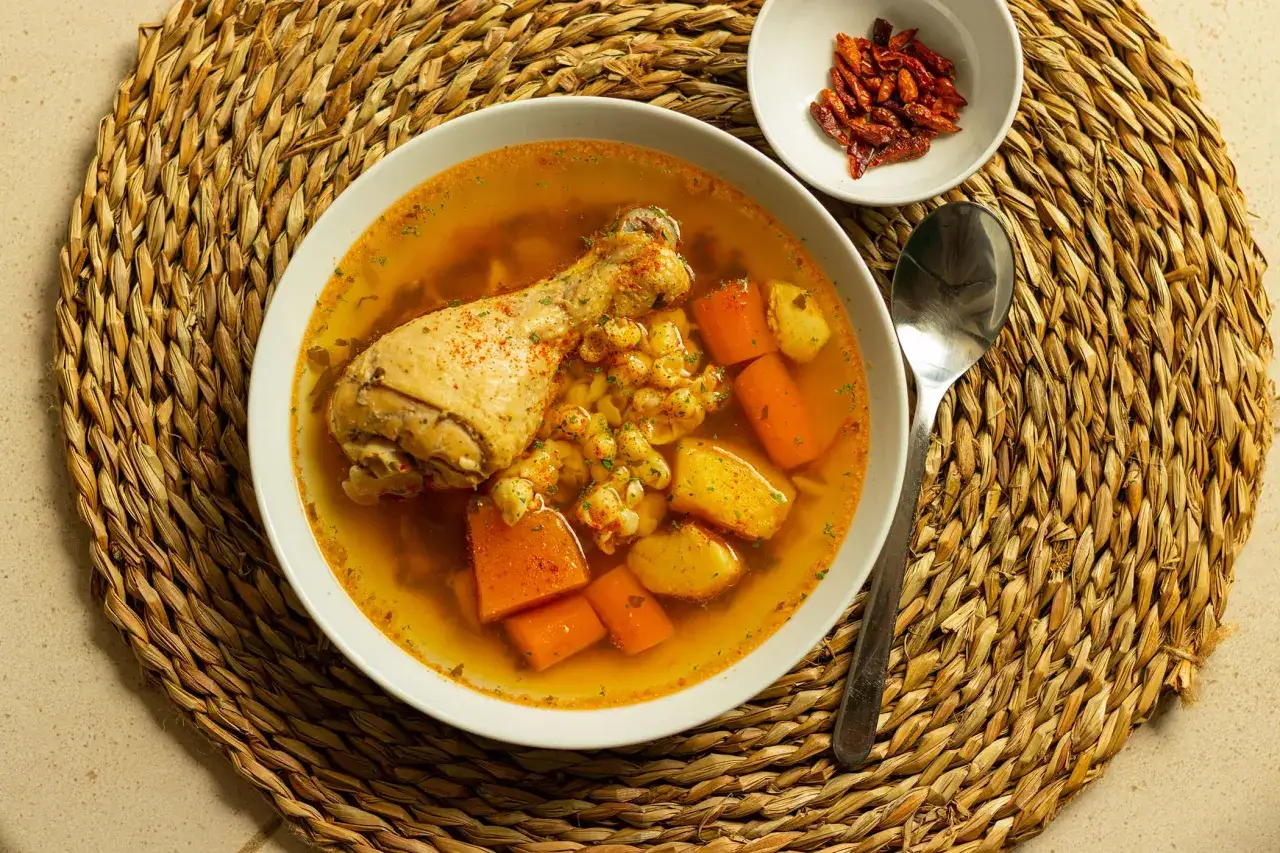 Un confortante brodo di pollo con pezzi di pollo, carote e patate. Accanto, una ciotolina di peperoncini secchi.
