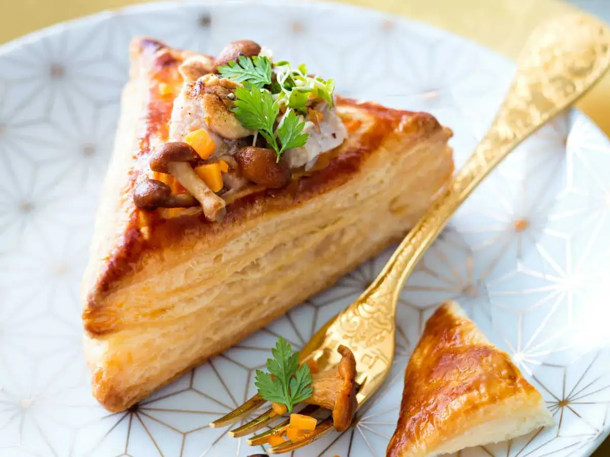 Délicieux feuilleté de ris de veau garni de champignons et de persil, servi sur une assiette ornée.