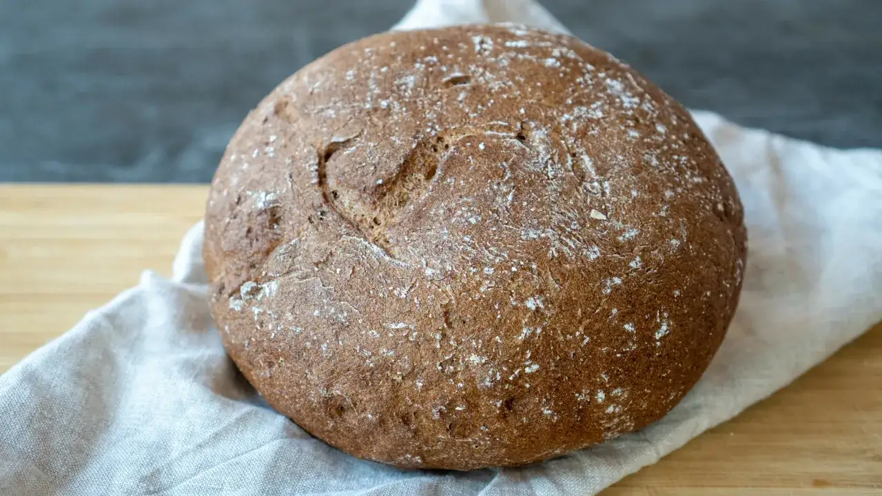 Ein rustikales Brot ohne Mehl, mit einer herzförmigen Vertiefung auf der Kruste, liegt auf einem Leinentuch.