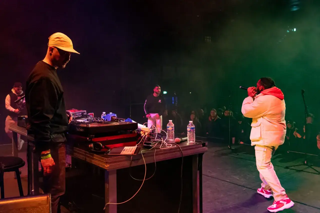 Un DJ hip hop aux platines, un rappeur au micro, et un public captivé par l'ambiance sur scène.