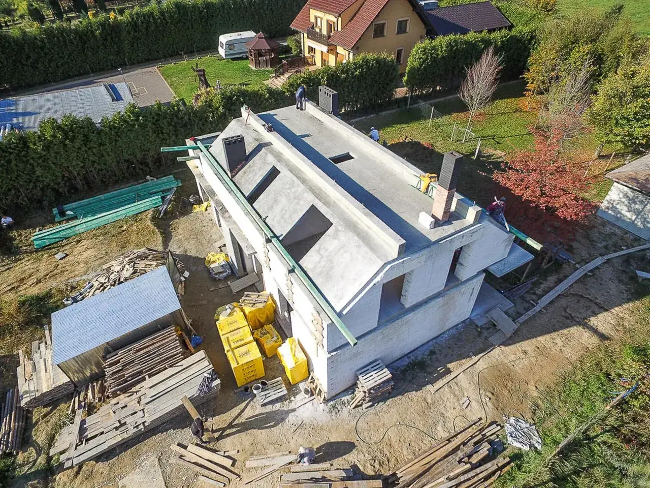 Budowa domu z betonowymi stropami i widocznymi lane skosy. Na placu budowy materiały budowlane i pracownicy.