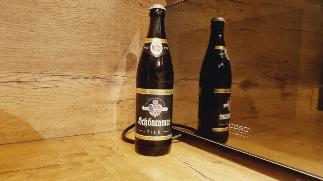 Schönramer Pils, ein Bier mit 35 IBU Hopfen, steht vor einer Holzvertäfelung. Sein Spiegelbild ist auf einer glänzenden Oberfläche zu sehen.
