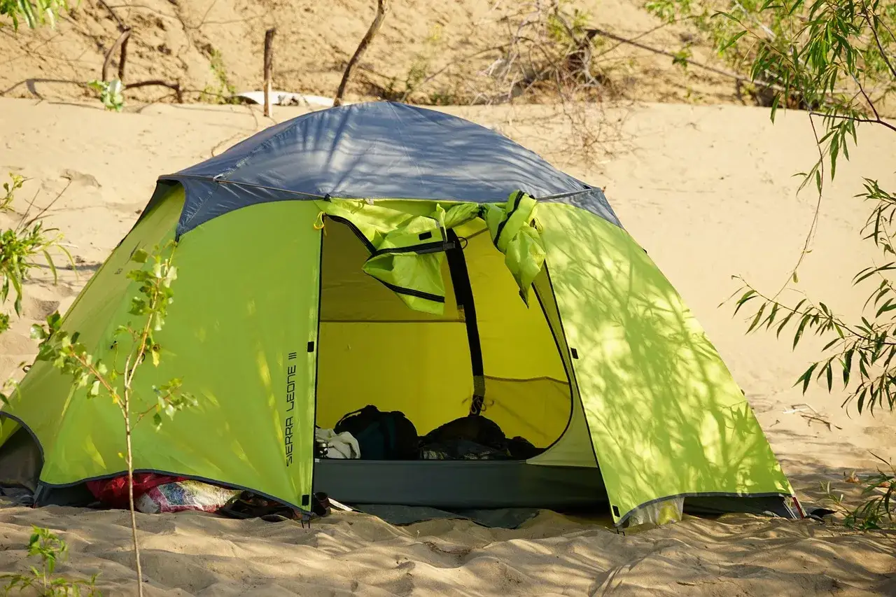 Tienda de campaña verde y gris en la arena, con bolsas dentro. ¡Espero que no sea una multa por acampar!