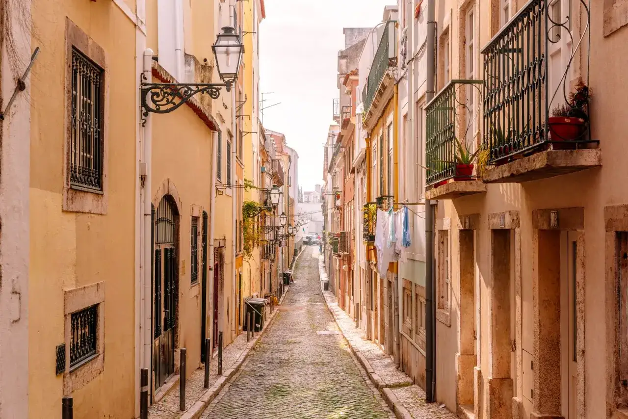 Enge Gasse in der **Lissabon Altstadt** mit Kopfsteinpflaster, bunten H&auml;usern und W&auml;sche, die zum Trocknen h&auml;ngt.