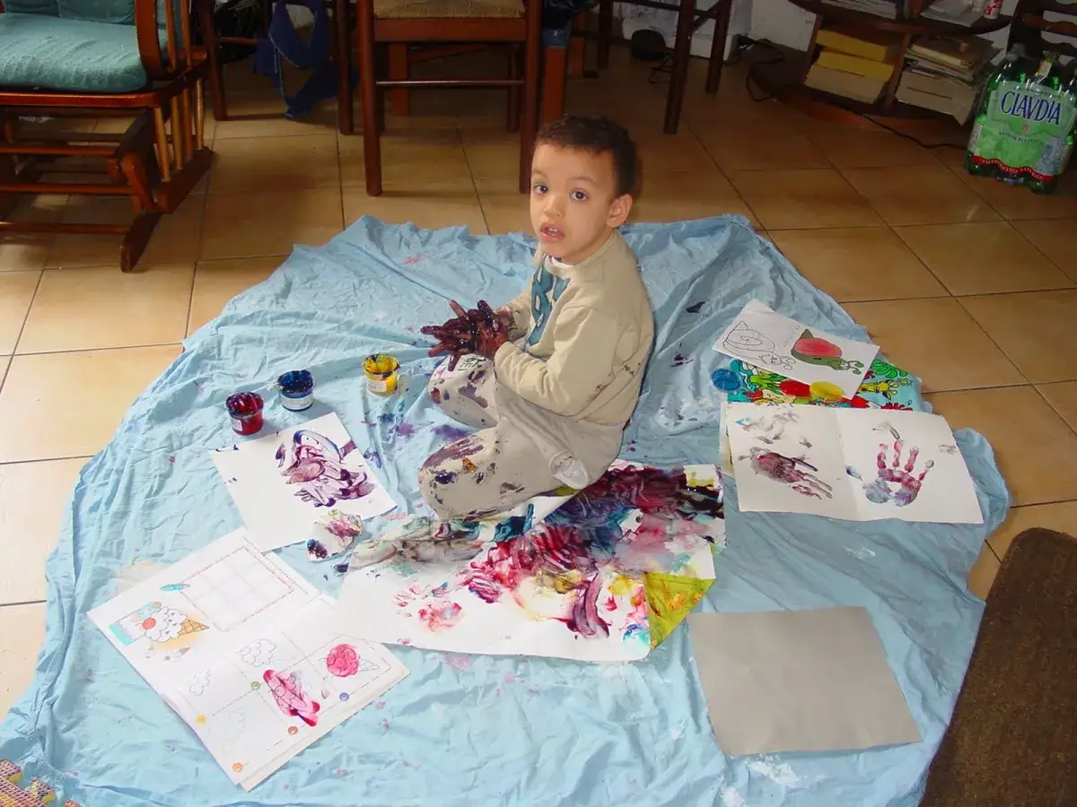 Bambino con mani dipinte esplora colori e texture, un'attività sensoriale per l'autismo.