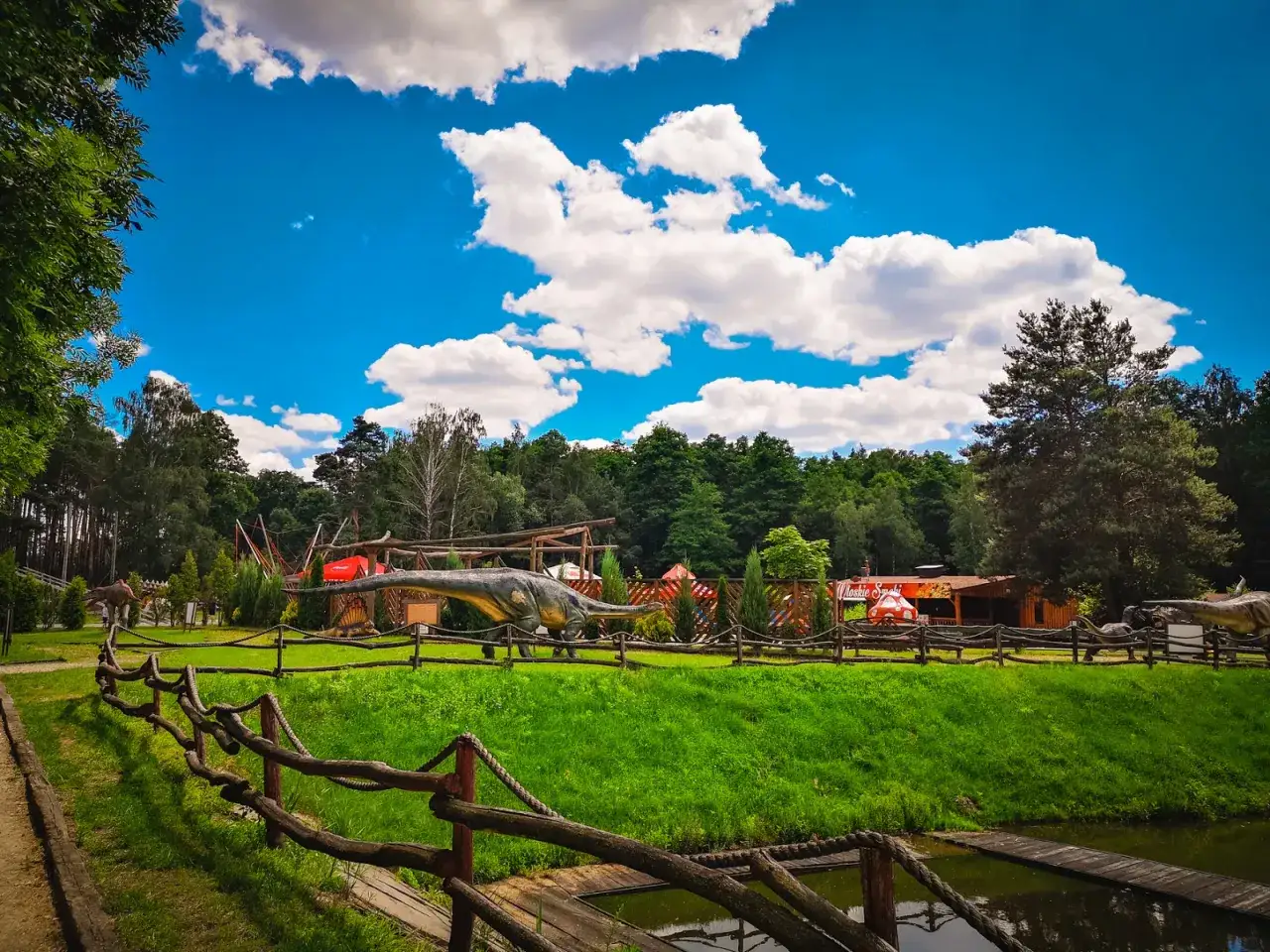 Park z dinozaurami, wspaniałe **ostrowskie wielkopolskie atrakcje** dla całej rodziny. Długoszyje stwory na tle zieleni i błękitnego nieba.