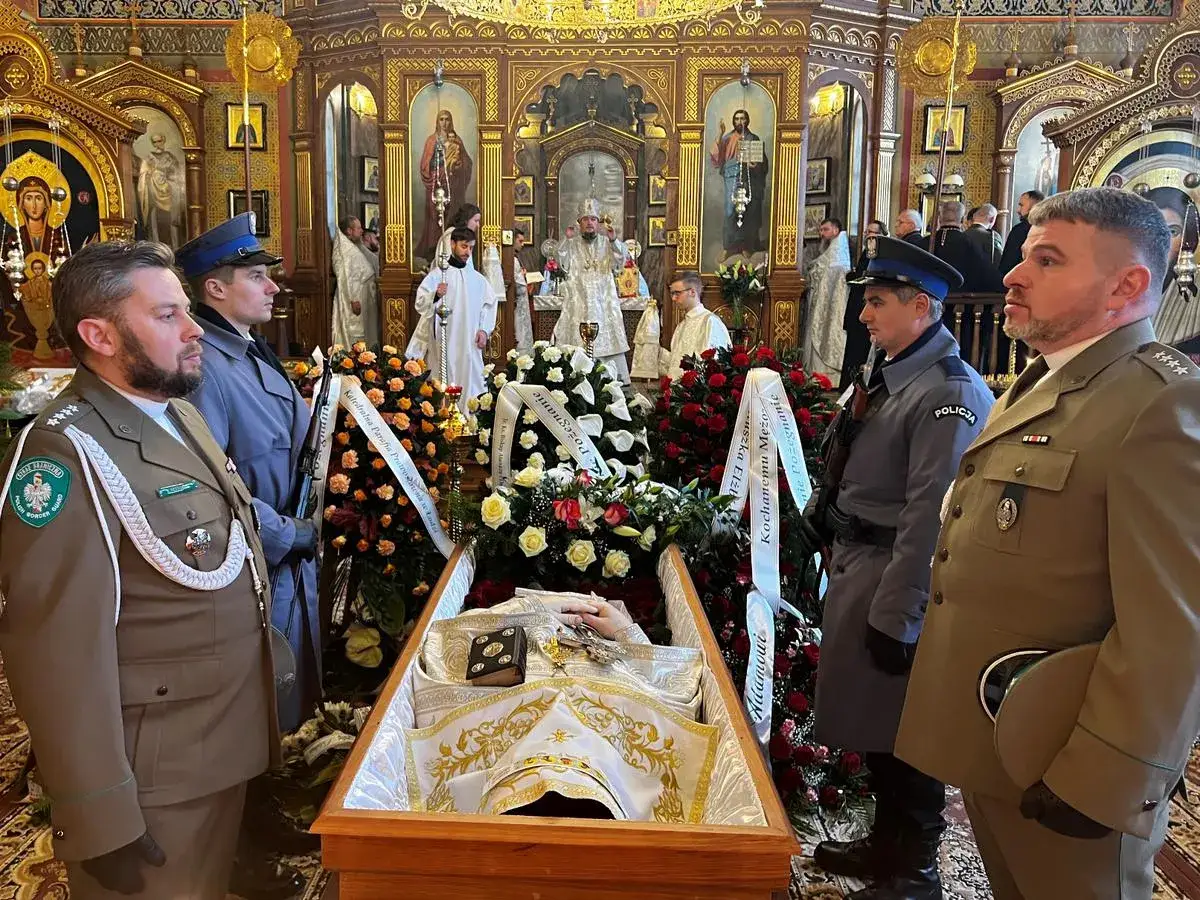 Uroczystość pogrzebowa w cerkwi. W żałobnej asyście, wśród kwiatów i ikon, spoczywa zmarły.