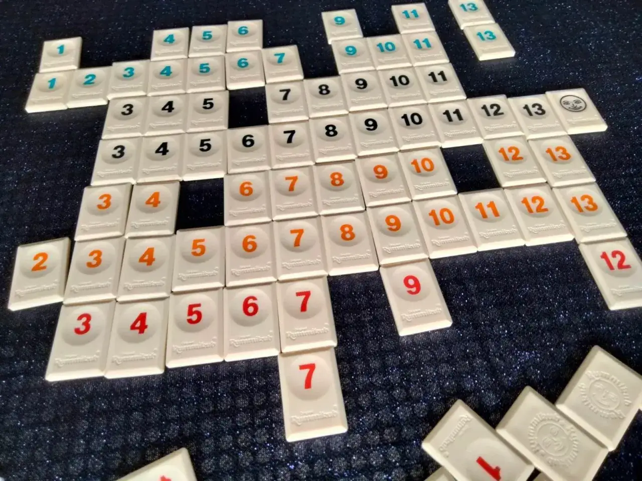 Klocki Rummikub ułożone w sekwencje i grupy, ilustrujące podstawowe zasady gry. Widoczne liczby od 1 do 13 w różnych kolorach.