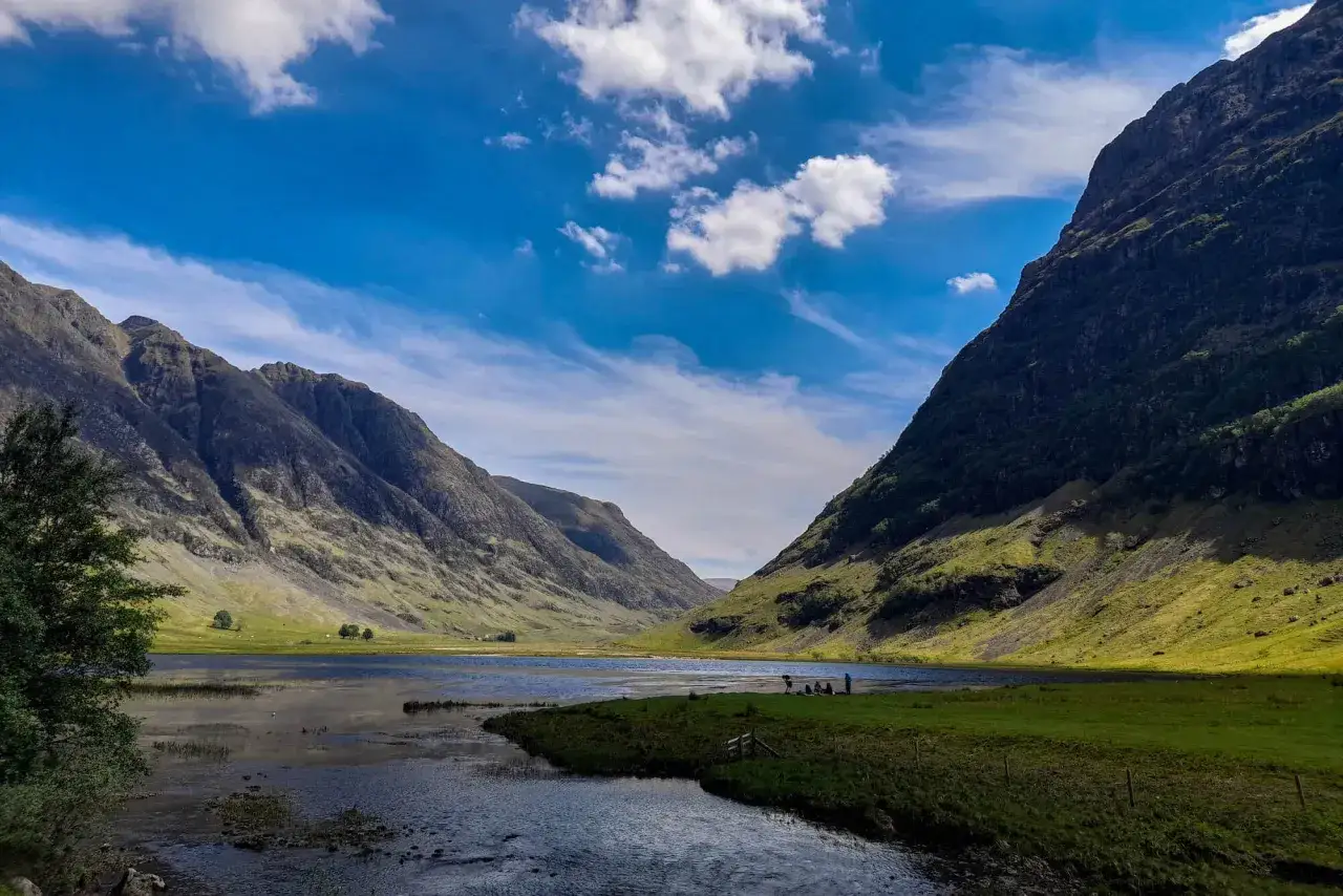 Un paisaje espectacular para hacer **escocia en bicicleta**. Montañas verdes, un lago sereno y cielo azul con nubes.
