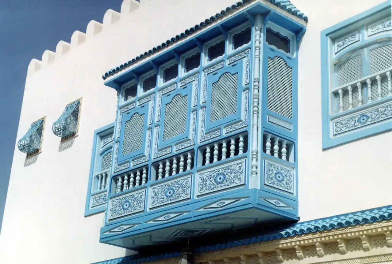Ein detailreiches arabisches Haus mit einem blauen, verzierten Erker und Gittern vor wei&szlig;em Putz.