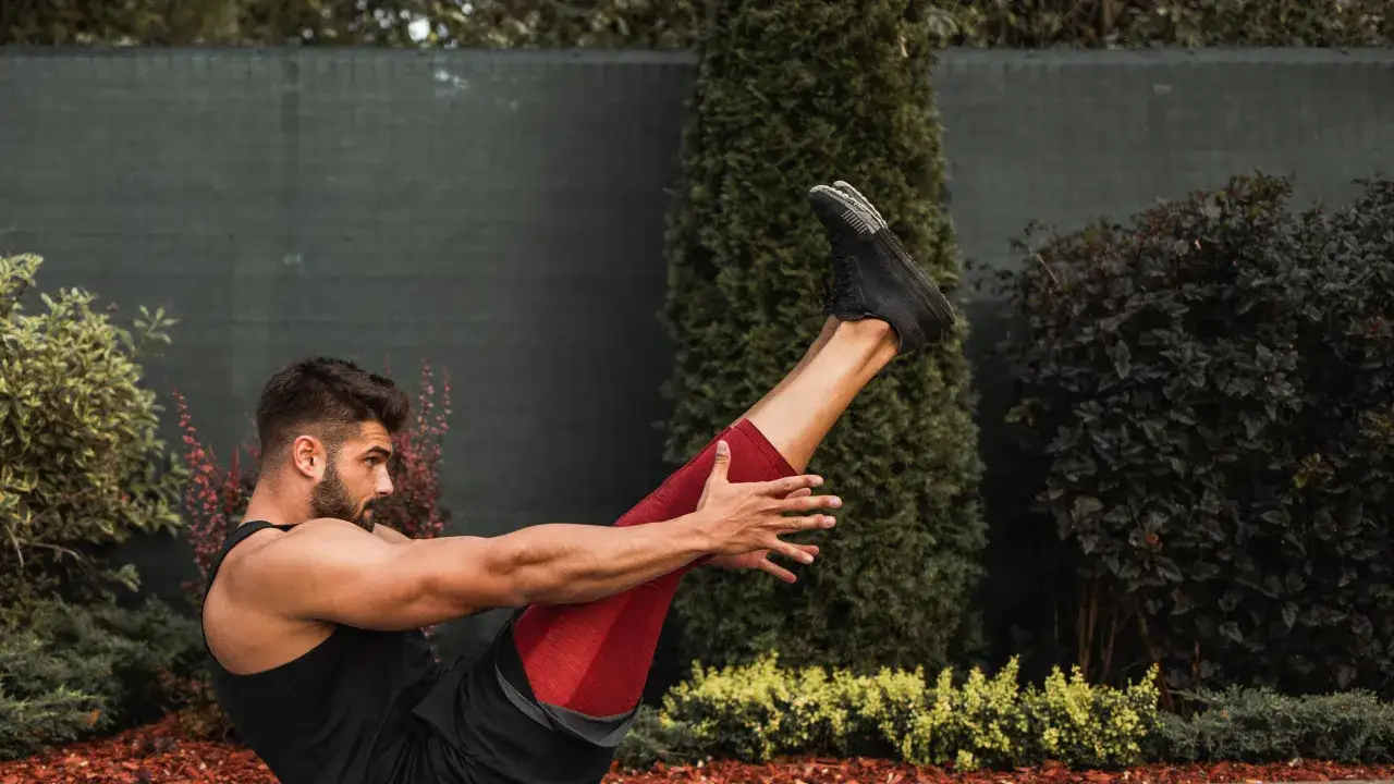 En stark yoga man tr&auml;nar utomhus, med benen lyfta i en balanserad position.