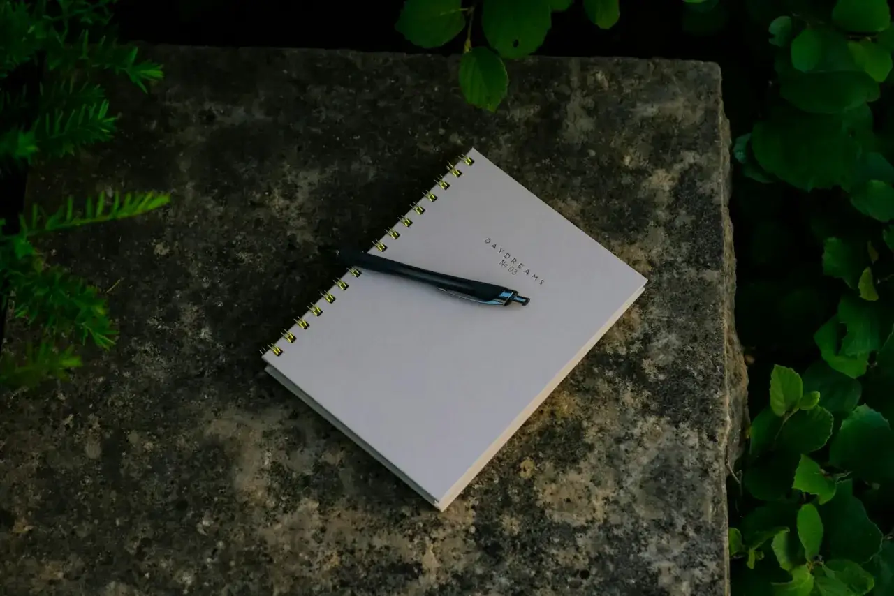 Notizbuch mit Stift auf Stein, umgeben von Grün. Ein Symbol für den **Neuanfang** in der **Psychologie**, um Gedanken und Träume festzuhalten.